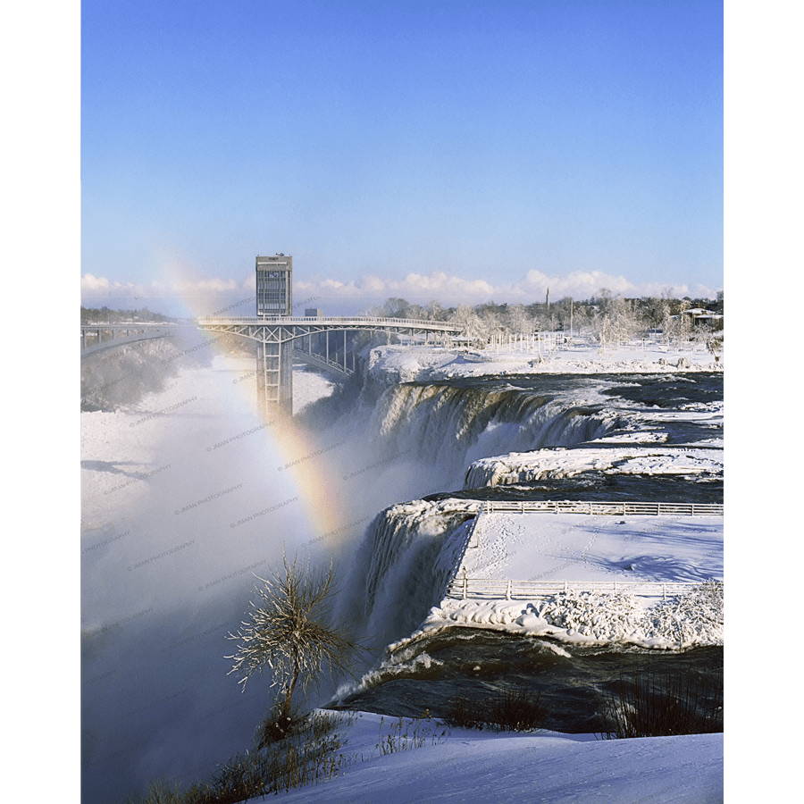 American Falls Winter Photo by Jman Photography shows a snow-covered Niagara Falls with a rainbow and observation tower, ideal for home or office decor.