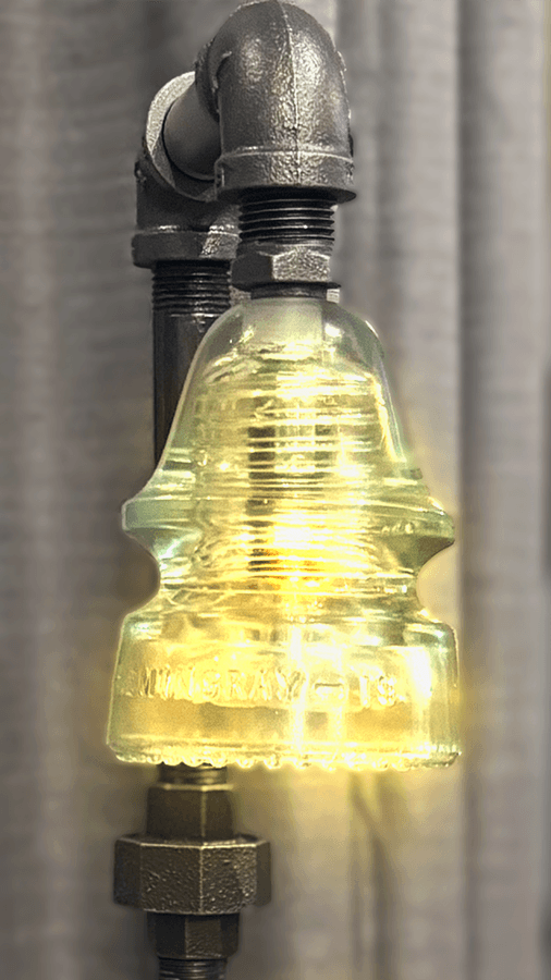 Glass insulator light fixture on Steampunk Industrial Lamp - Jingle Elephant | Illuminated vintage glass bulb mounted on pipe rail.