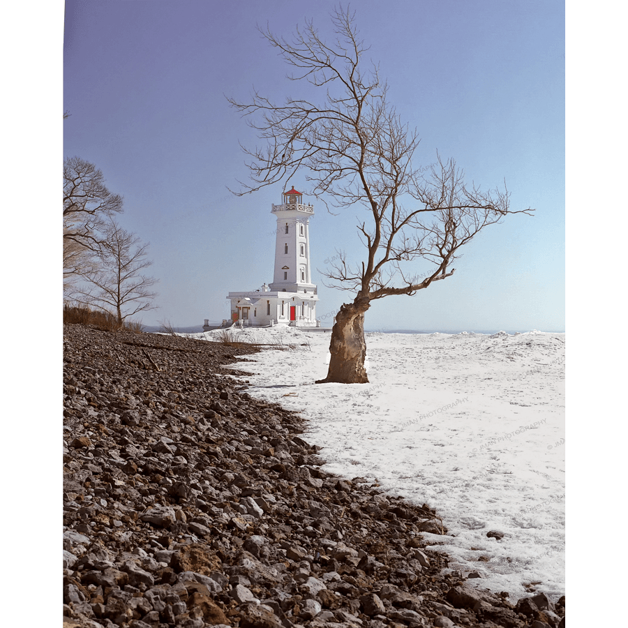 Point Abino Lighthouse Photo by Jman Photo shows a historic white lighthouse on Lake Erie's snowy shoreline with a leafless tree in the foreground.