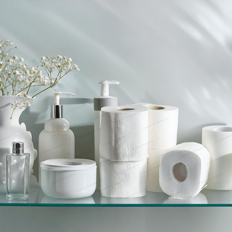 Close-up of porcelain-themed bathroom wall art with toilet paper, lotion bottles, and flowers. Unique decor accent for stylish bathroom spaces.