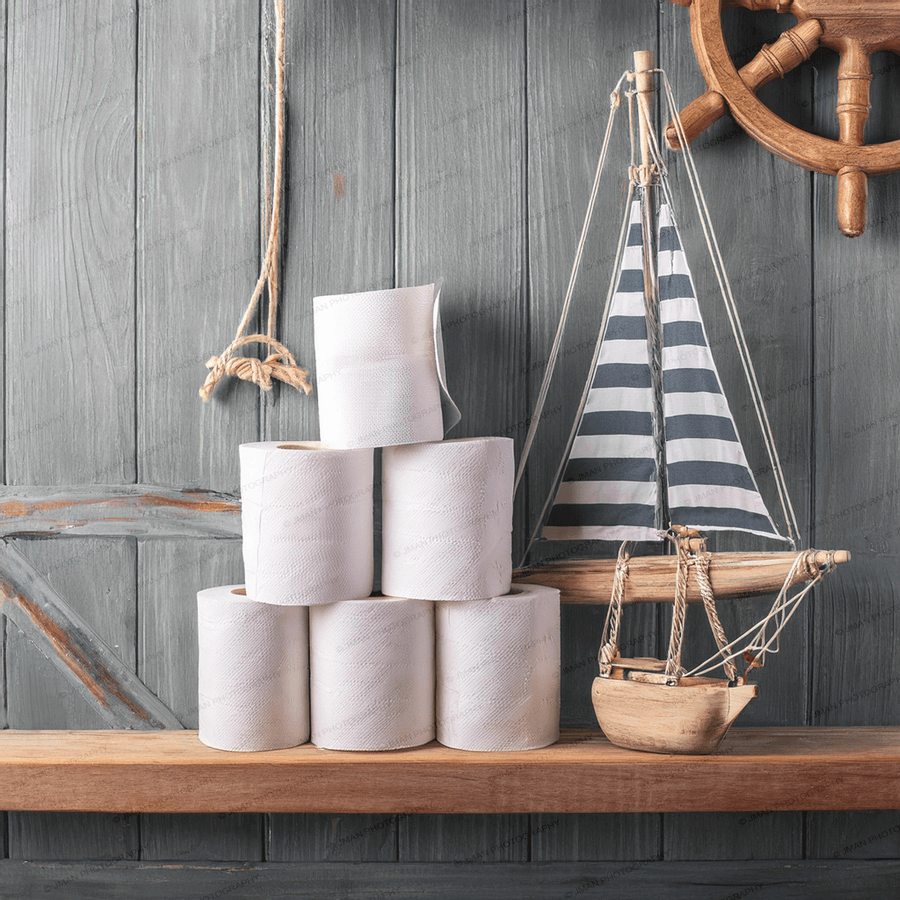 Sailboat Theme Roll of Toilet Paper Bathroom Wall Art featuring stacked toilet paper rolls beside a decorative sailboat and ship wheel on wooden shelf.