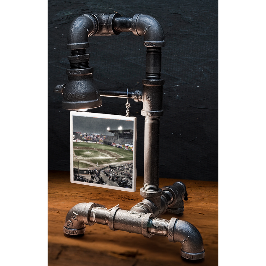 Industrial-style table lamp made from black metal pipes with a small framed baseball stadium photo hanging from the pipe, on a wooden surface