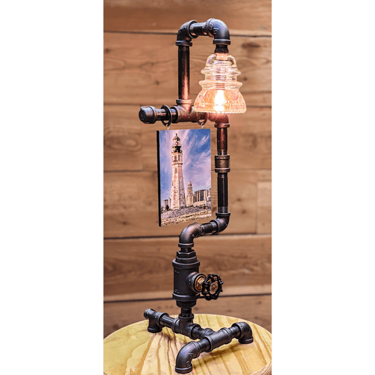 Steampunk Lamp with Insulator features a clear glass insulator light, 5x7 lighthouse photo, and valve switch on black iron pipe base. Ideal for vintage decor.