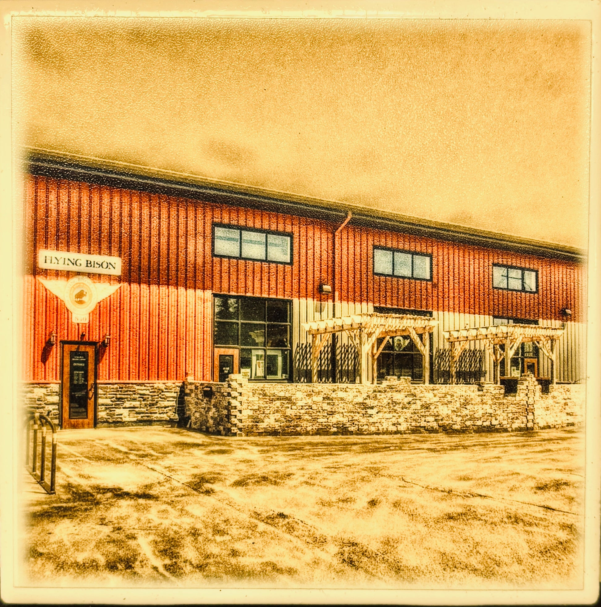 A  photograph of a red metal building with large windows, a stone foundation, and a sign reading 'FLYING BISON.' This appears to be a real outdoor architectural scene rather than a clean product shot, chart, swatch, or instruction graphic.