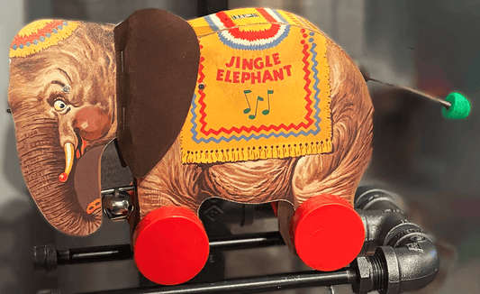 Close-up of Jingle Elephant toy on Steampunk Industrial Lamp, showcasing vintage design with red wheels and colorful detailing.